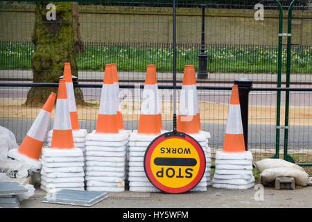 Stacked traffic cones and a stop work sign on the  side of a fenced off road Stock Photo