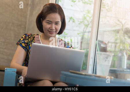 Young Asian woman working online at home with laptop computer. Freelance and outsource worker activity concept. Stock Photo