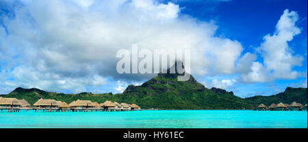 Panorama image of a tropical Bora Bora landscape with green Otemanu mountain behind a luxury resort in the turquoise lagoon of the island near Tahiti  Stock Photo