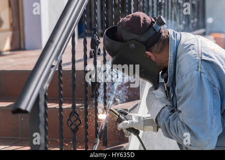 A worker welding metal handrails on the stairs. Wrought iron railings. Private house. Ukraine. Stock Photo