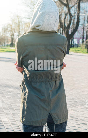 View from the back of a sporty woman in a hood getting ready to run in the park in the morning, vertical framing Stock Photo