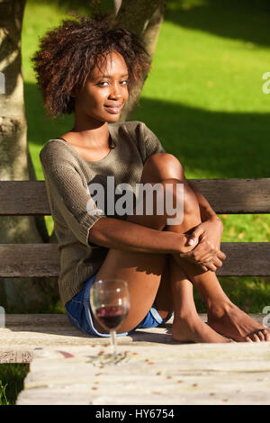 Portrait of a young african american woman sitting barefoot in park Stock Photo
