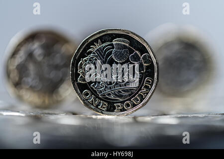 new pound coin introduced in Britain in 2017, front, standing on a layer of coins within two other coins in the distance (trio) Stock Photo