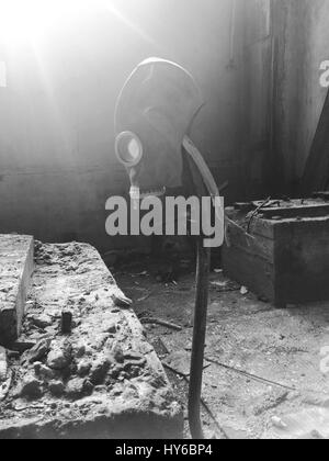 Black and white photo gas mask hanging on a vertical stick in an abandoned building Stock Photo