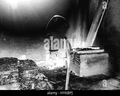 Black and white photo gas mask hanging on a vertical stick in an abandoned building Stock Photo