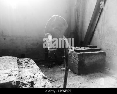 Black and white photo gas mask hanging on a vertical stick in an abandoned building Stock Photo