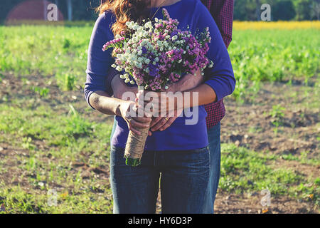 Young loving couple outdoor, holding hands. Man gifting a flower bouquet to his girlfriend. Natural sunset light, focus on hands and flowers. Stock Photo