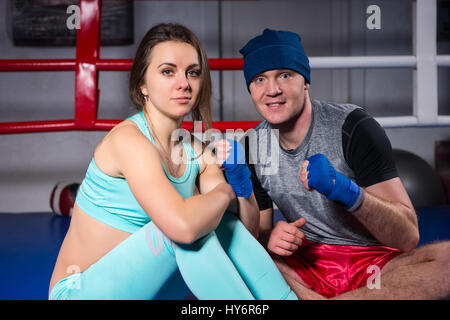 Smiling young boxing couple preparing bandages sitting in regular boxing ring in a gym Stock Photo