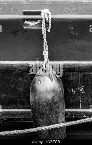 Black and white image of a plastic fender hanging by a rope on the side of a narrowboat moored on Regent's Canal, King's Cross, London, UK Stock Photo