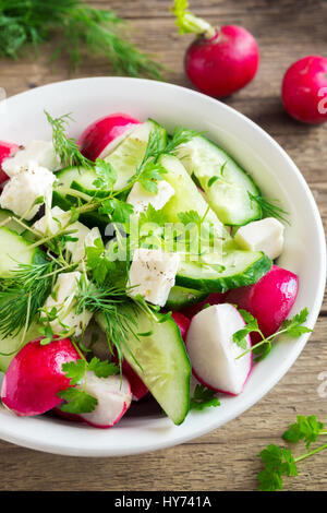 Spring vegetable salad with fresh cucumber, radishes, feta cheese, herbs, sprouts in bowl on wooden background - healthy detox organic diet vegan vege Stock Photo