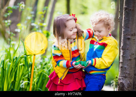 Children playing outdoors. Preschool kids catching frog with net. Boy and girl fishing in forest river. Adventure kindergarten day trip into wild natu Stock Photo