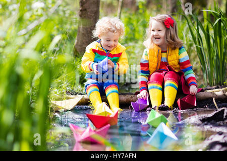 Children play with colorful paper boats in a small river on a sunny spring day. Kids playing exploring the nature. Brother and sister having fun at a  Stock Photo