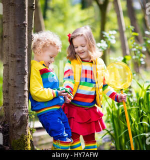 Children playing outdoors. Preschool kids catching frog with net. Boy and girl fishing in forest river. Adventure kindergarten day trip into wild natu Stock Photo