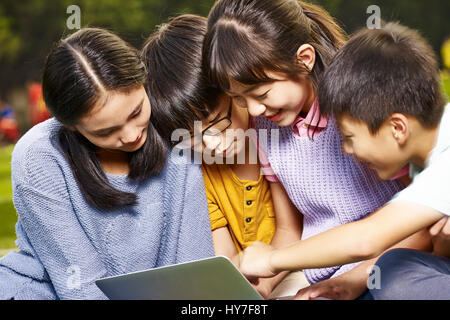 asian elementary schoolgirls and schoolboys using laptop computer together outdoors. Stock Photo