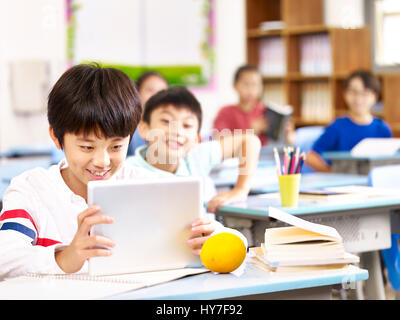 asian elementary school child using tablet computer in classroom, happy and smiling. Stock Photo