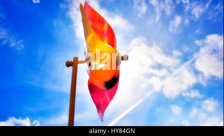 Colorful toy windmill against the sun and a blue sky. Stock Photo