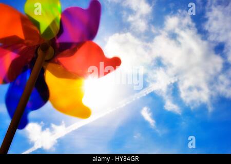 Colorful toy windmill against the sun and a blue sky. Stock Photo