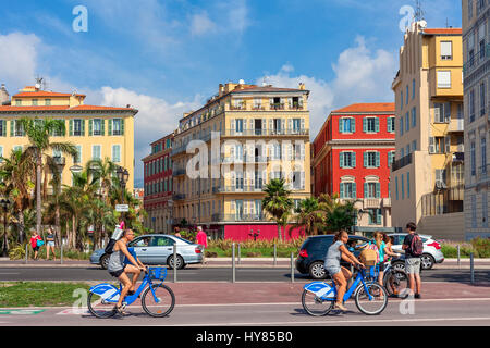 NICE, FRANCE - SEPTEMBER 04, 2016: People on rental city bicycles ride on Promenade des Anglais as colorful buildings on background in Nice - city loc Stock Photo