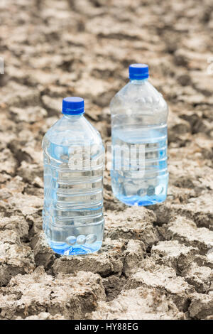 Bottle with water on the dried ground. Concept of Global drought, warming. Dried soil. lack of water, thirst concept. Stock Photo