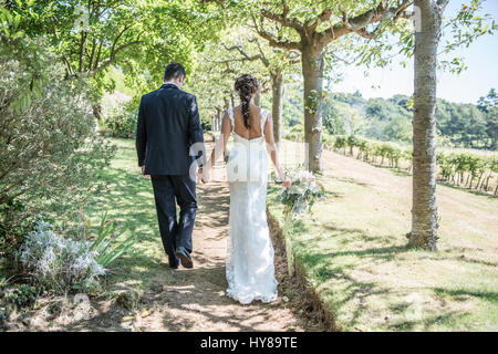 A bride and groom walk along hand in hand on their wedding day Stock Photo