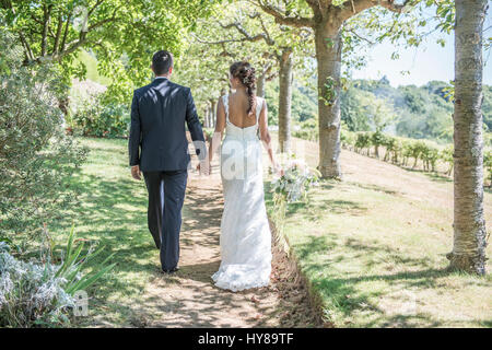 A bride and groom walk along hand in hand on their wedding day Stock Photo