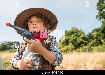 A young boy plays cowboys and indians outside in the sunshine Stock Photo