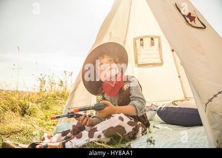 A young boy plays cowboys and indians outside in the sunshine Stock Photo