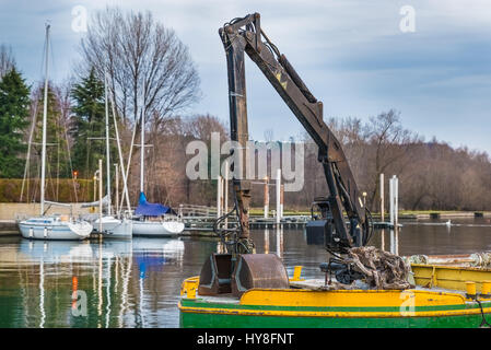 Small dredge floating in the harbor of a lake. Machine for the excavation, the collection of material, the cleaning the mud from the bottom Stock Photo