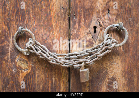Old rusted padlock, rusted chain, and keyhole on a closed wooden aged grunge double door Stock Photo