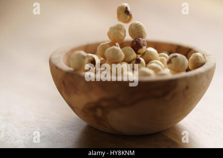 roasted hazelnuts falling in wood bowl on wooden table, closeup photo Stock Photo