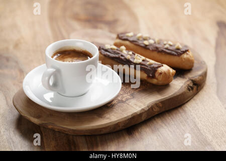 fresh espresso and eclairs with hazelnuts on wood table, sweet morning breakfast Stock Photo