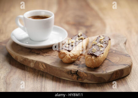 fresh espresso and eclairs with hazelnuts on wood table, sweet morning breakfast Stock Photo