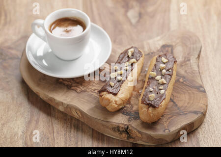 fresh espresso and eclairs with hazelnuts on wood table, sweet morning breakfast Stock Photo