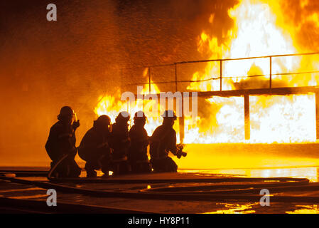 Group of firefighters spraying down burning structure during firefighting exercise Stock Photo