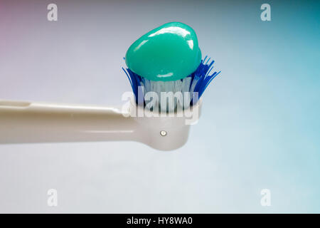 Close-up on the side of a worn-out white and blue head of an electric toothbrush topped with blue toothpaste, against a blue gradient - oral hygiene c Stock Photo