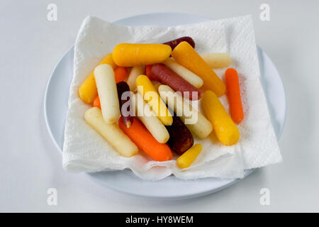 Closeup on plate of baby rainbow carrots on white paper towel on plate against white background- healthy eating concept Stock Photo