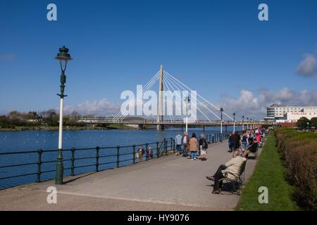 People walking by Marine Boating lake in Southport with Marine Way bridge and pier in distance Stock Photo