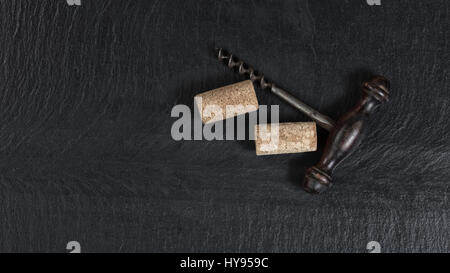 Overhead view of antique wine corkscrew and used corks on black slate Stock Photo