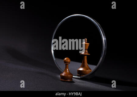 Pawn looking in the mirror and seeing a king. Black background. Stock Photo
