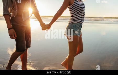 Cropped shot of young couple holding hands and walking on the beach. Loving man and woman strolling on the shore. Stock Photo