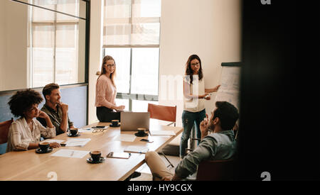 Female executive explaining new business strategy to colleagues in conference room. Business people discussing in meeting room at office. Stock Photo