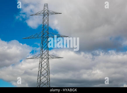 Looking up to top of tall electricity pylon tower with overhead cables against a blue sky with white fluffy clouds, Scotland, UK Stock Photo