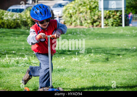 A young boy riding a push scooter in the park. Stock Photo