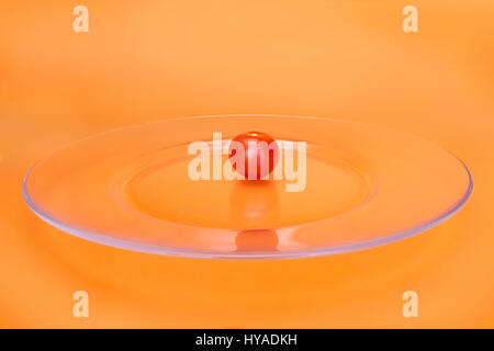 Small red cherry tomato on transparent glass plate. On abstract orange background, selective focus Stock Photo