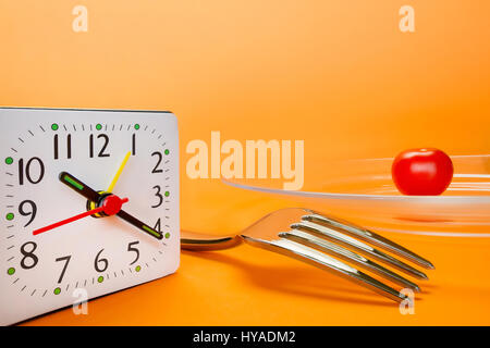 Alarm clock, fork and small cherry tomato on abstract orange background. Diet and lunch time concept Stock Photo