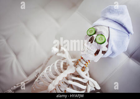 Skeleton in Spa salon with towel on her head and mask on her face, relaxes. An absurd concept, social parody. Take care of beauty and forget about inn Stock Photo