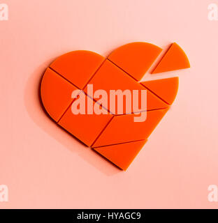 Plastic puzzle in the form of heart with disconnected piece on a pink background Stock Photo