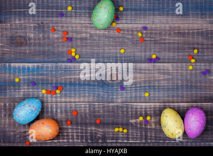 Colored Easter eggs are scattered on a wooden background. Place for text in the center Stock Photo