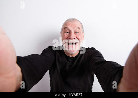 Senior man in black t-shirt, taking selfie, studio shot. Stock Photo