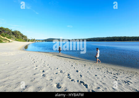 Two persons walking along the sandy shores of Lake Conjola, Shoalhaven, South Coast, New South Wales, NSW, Australia Stock Photo